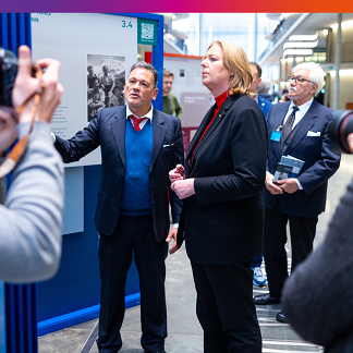 Foto: Kurator Karl-Heinz Steinle steht mit Bundestagspräsidentin Bärbel Bas vor einer Ausstellungswand. Steinle zeigt mit der Hand auf etwas. Bärbel Bas hört mit ernstem Gesichtsausdruck zu. Im Hintergrund sind verschwommen weitere Ausstellungswände zu sehen.