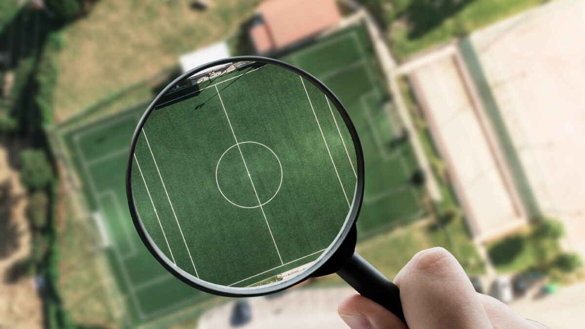 Foto aus Vogelperspektive mit Fußballfeld und Lupe.