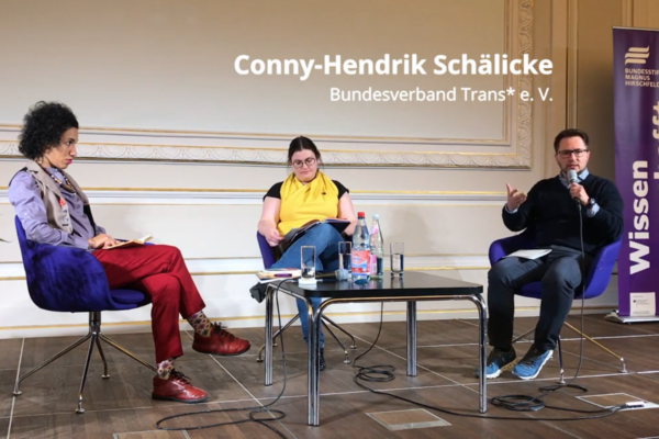 Screenshot des Videos “Gedenkveranstaltung: Ausgelöscht. Verloren. Wiederentdeckt”. Zu sehen sind drei Referent_innen, die auf einem Podium um einen Tisch sitzen.