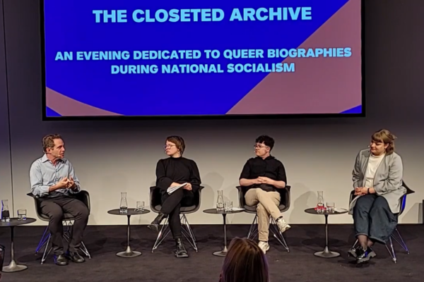 Screenshot des Videos “The Closeted Archive. An Evening Dedicated to Queer Biographies during National Socialism”. Zu sehen sind vier sitzende Personen auf einem Podium. Projektion des Veranstaltungstitels über den Personen.