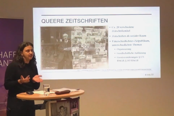 Screenshot des Videos „Vortrag: Verflochtene Imaginationen: Geschlecht, Sexualität und Kolonialität in queeren deutschen Zeitschriften des frühen 20. Jahrhunderts“. Zu sehen ist Leo Ryczko vor einer Folie seiner Präsentation.