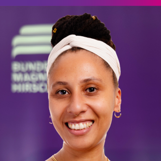 Portraitfoto Pamela Akosua Twinwaah Amponsah Im Hintergrund ist verschwommen das Logo der Bundesstiftung Magnus Hirschfeld in weiß vor lila Hintergrund zu erkennen.